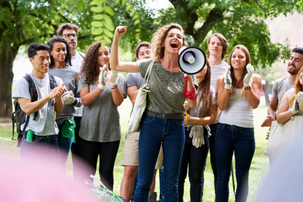 Young female volunteer with her fist up while talking on megaphone while other volunteers are standing in background during garbage cleanup program